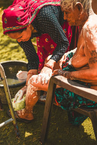 Daughter bathing her old mother in yard