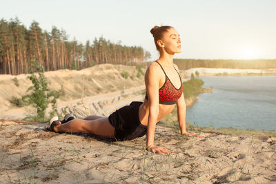 Woman in sports clothing exercising at beach during sunset