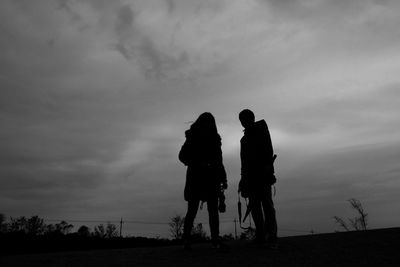 Silhouette people standing on landscape against clouds