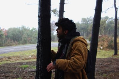 Side view of young man standing in forest