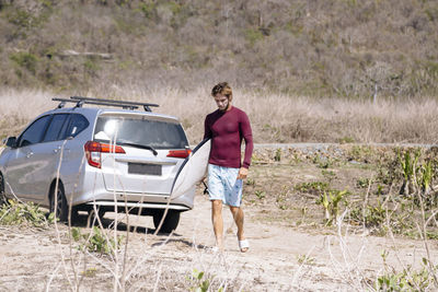 Young man with surfboard near car