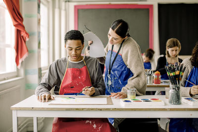 Young female teacher guiding male teenage student during art class at high class