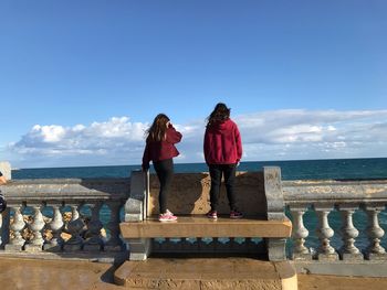 Rear view of women standing by sea against blue sky