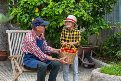 Senior man, farmer, worker with a young boy holding in hands harvest of organic fresh tomato