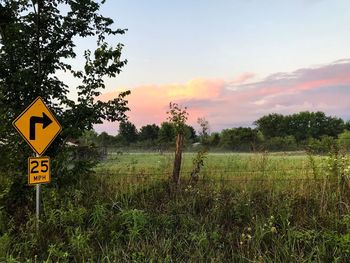 Road sign on field against sky