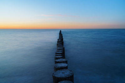 Wooden posts in sea against sky during sunset