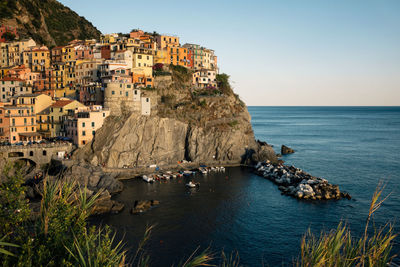 Buildings on cliff by sea against sky at manarola