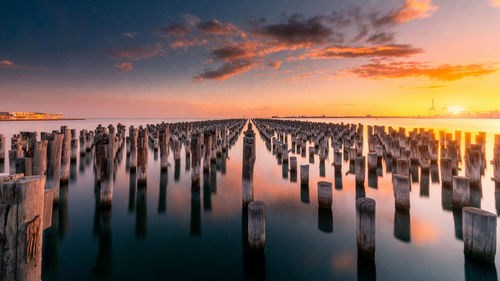 Panoramic view of wooden posts in sea against sky during sunset