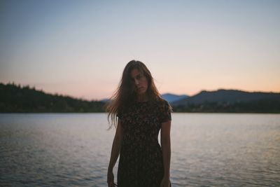 Portrait of woman standing at lakeshore at sunset