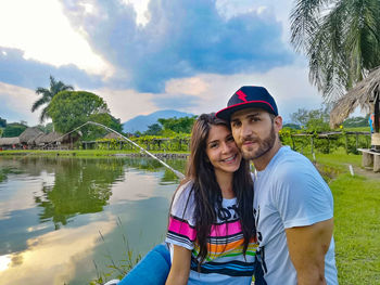 Portrait of smiling young couple by lake against sky