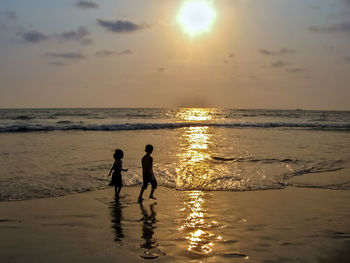 Silhouette people on beach against sky during sunset