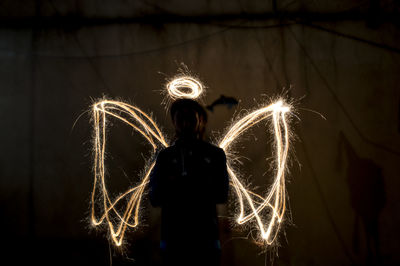 Silhouette man standing against lighting painting making angel wings and halo in dark