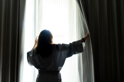 Rear view of woman standing by window at home