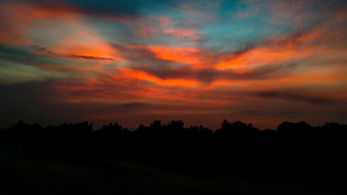 Silhouette trees against dramatic sky during sunset