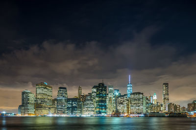 River and illuminated buildings against cloudy sky at dusk