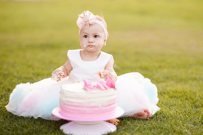 Baby girl 1 year old wear princess dress eating birthday cream cheese cake sitting on grass