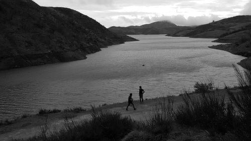 High angle view of silhouette male friends standing at lakeshore against mountains