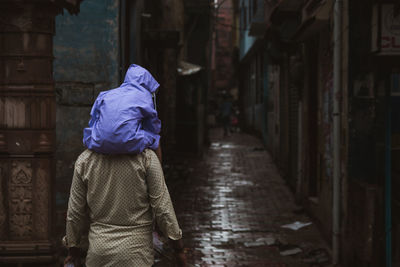 Rear view of man carrying baby on shoulder in alley