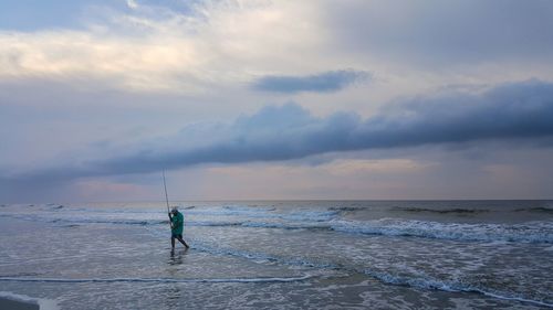 Man walking at beach against cloudy sky