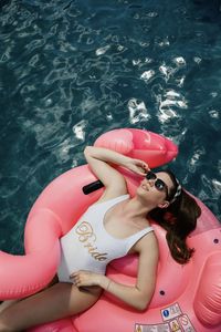 High angle view of woman floating in swimming pool on pink flamingo