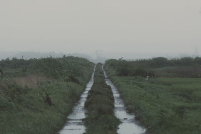 Dirt road amidst field against sky