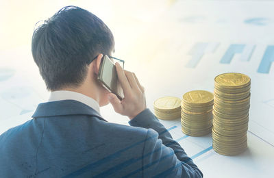 Digital composite image of businessman using mobile phone by stacked coins