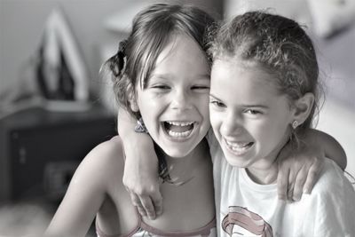 Close-up of happy sisters with arms around standing at home