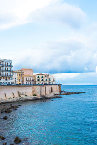 Buildings by sea against sky