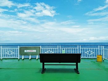 Empty bench by sea against sky