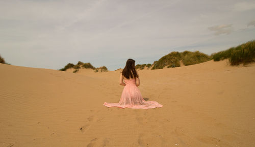 Low angle view of young woman kneeling on sand dune at beach