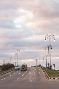 Vehicles on road against cloudy sky