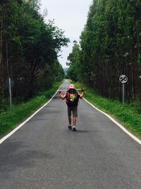 Rear view of man walking on road amidst trees