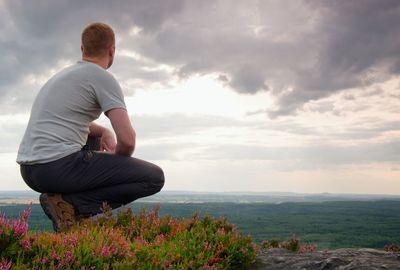 Hiker in squatting position on a rock in heather bushes, enjoy the scenery