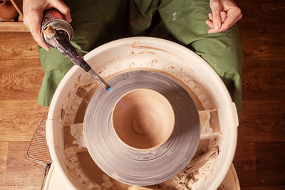 A female potter in a green apron and a plaid shirt sculpts a clay vase from clay on a potter's wheel