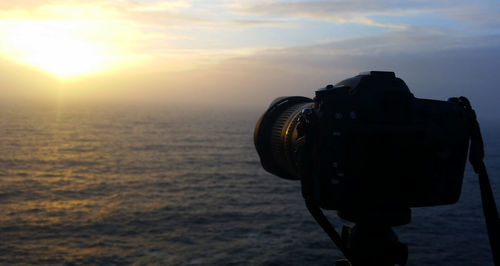 Reflection of camera on sea against sky during sunset