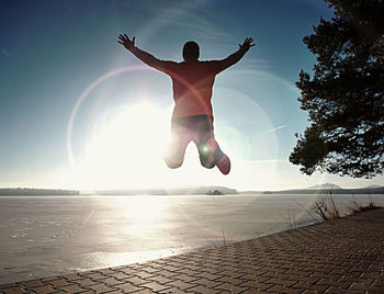 Full length of woman jumping on beach against sky during sunset