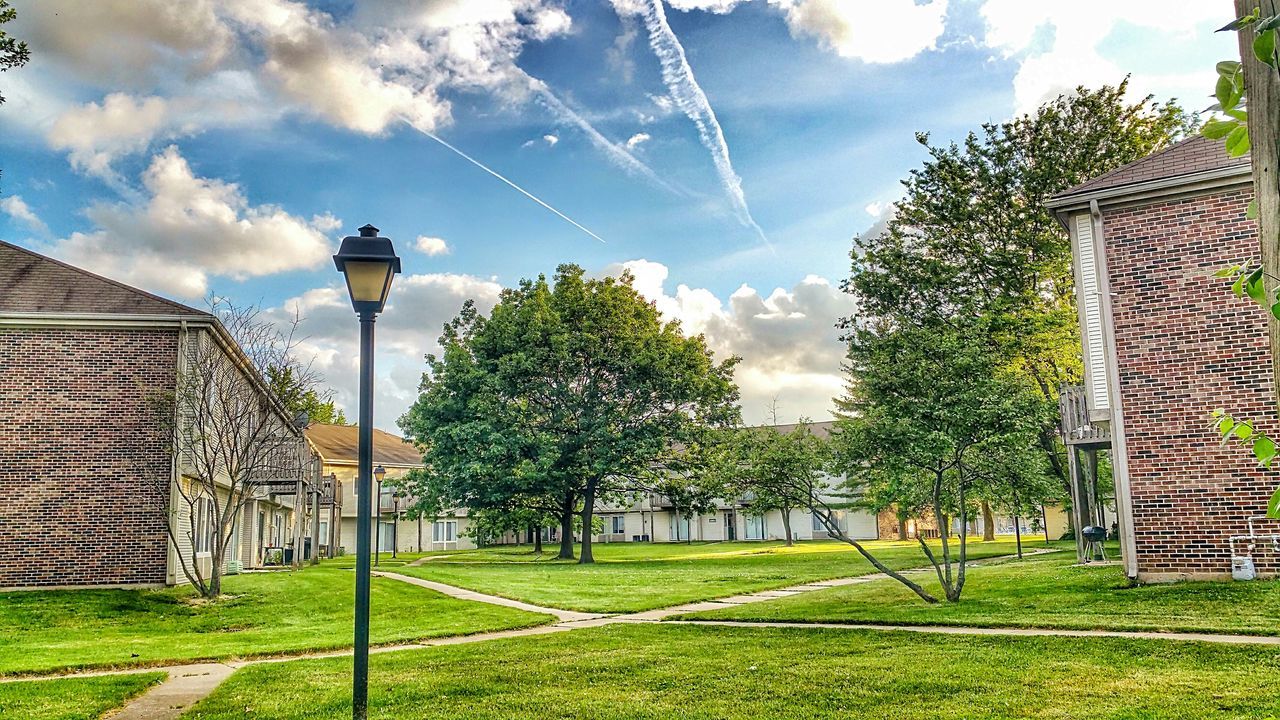grass, sky, building exterior, architecture, built structure, tree, green color, street light, cloud - sky, growth, cloud, grassy, field, fence, sunlight, nature, lighting equipment, day, park - man made space, outdoors