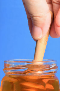 Close-up of hand holding glass jar against blue background