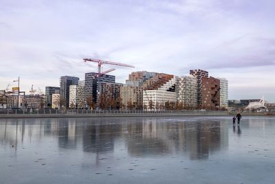 Buildings by frozen lake in city against sky