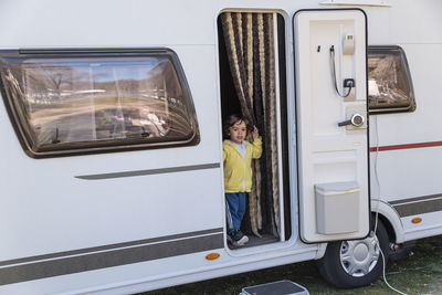 Curly haired boy at the door of his motorhome on a sunny morning.