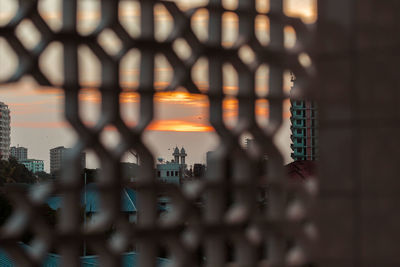 Digital composite image of chainlink fence and buildings against sky during sunset