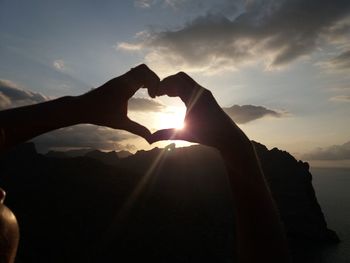 Close-up of silhouette hands making heart shape against sky during sunset