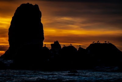 Silhouette of rocks at sea during sunset