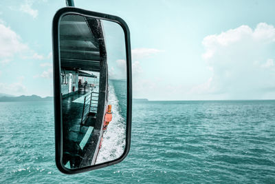 Side-view mirror of boat over sea against sky