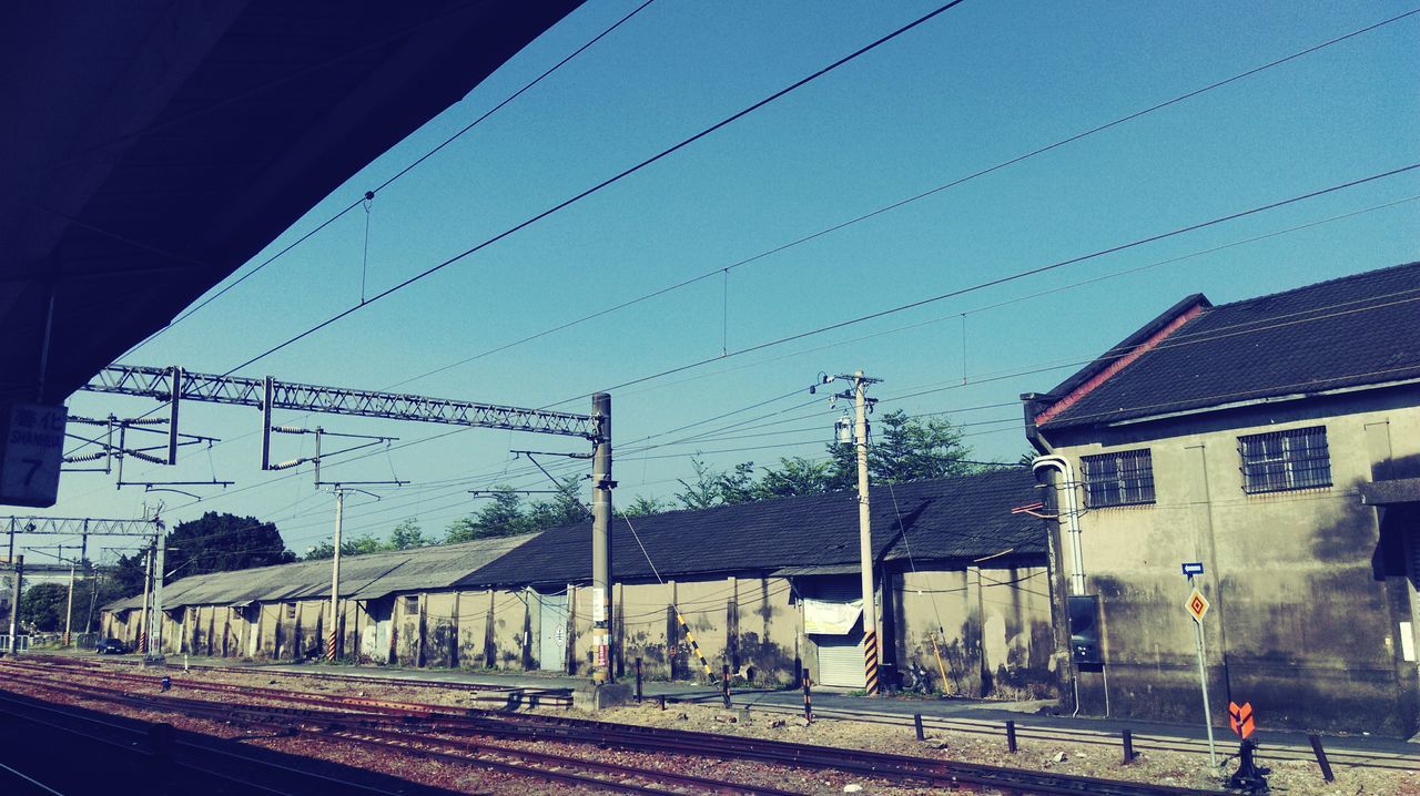 railroad track, transportation, rail transportation, public transportation, building exterior, built structure, architecture, power line, railroad station platform, railroad station, electricity pylon, train - vehicle, sky, cable, blue, railway track, the way forward, clear sky, mode of transport, road