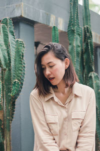 Young woman looking away while standing against plants