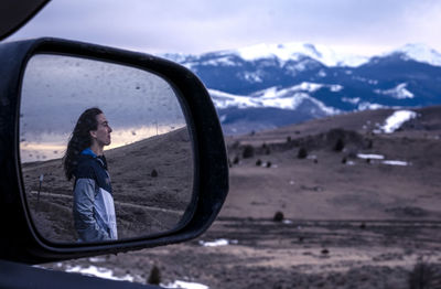 Young woman looking at sunset in the mountains reflected in mirror