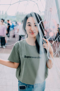 Portrait of smiling young woman standing amidst net outdoors