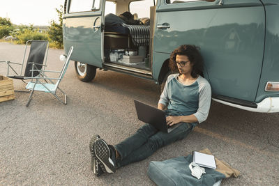 Man using laptop sitting against camping van