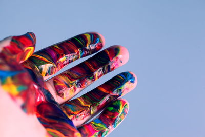 Close-up of cropped hand with watercolor paints against clear sky